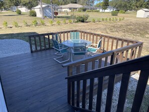 A wooden deck with a glass table and chairs, surrounded by a wooden railing.