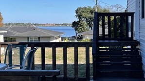 Une terrasse en bois offrant une vue sur une étendue d’eau, avec une maison en arrière-plan.