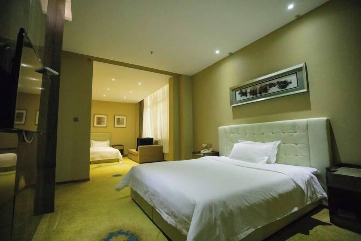 A hotel room with a large bed, a bedside table, a chair, and a framed picture on the wall.