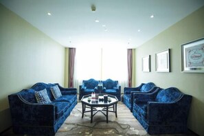 Une pièce avec deux canapés en velours bleu, une table basse en verre et une grande fenêtre avec des rideaux.