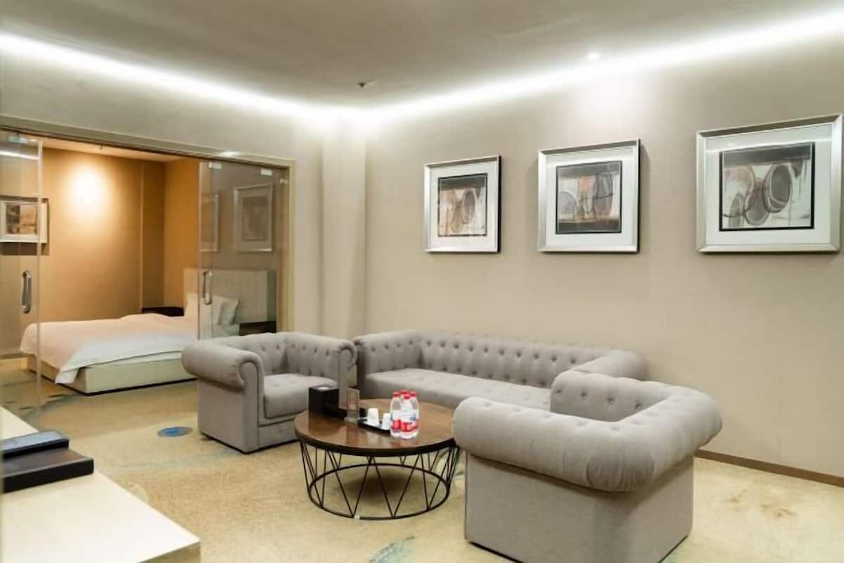 A hotel room with a sectional sofa, a round coffee table, a bed, and three framed pictures on the wall.