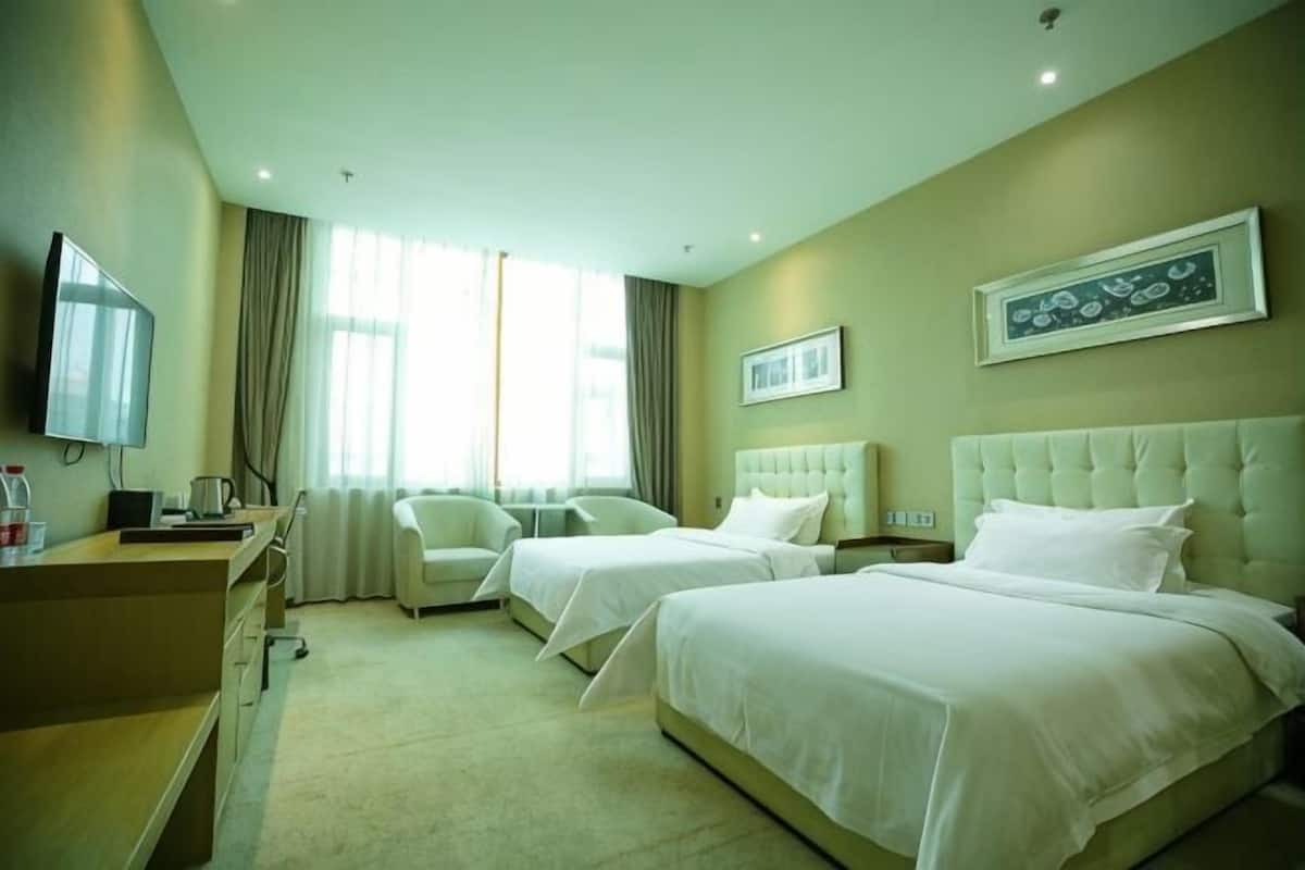 A hotel room with two beds, a desk, a chair, a TV, and a large window.