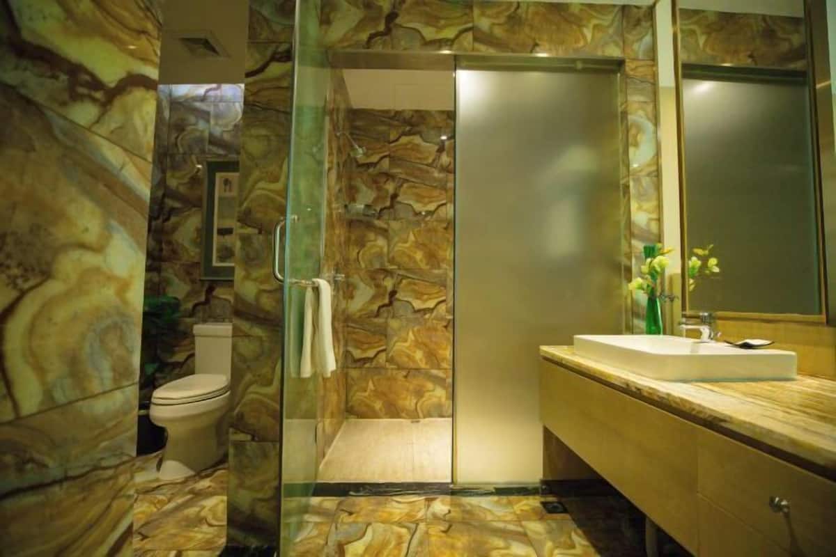 A bathroom with a marble wall, a glass shower enclosure, a toilet, and a sink with a mirror.