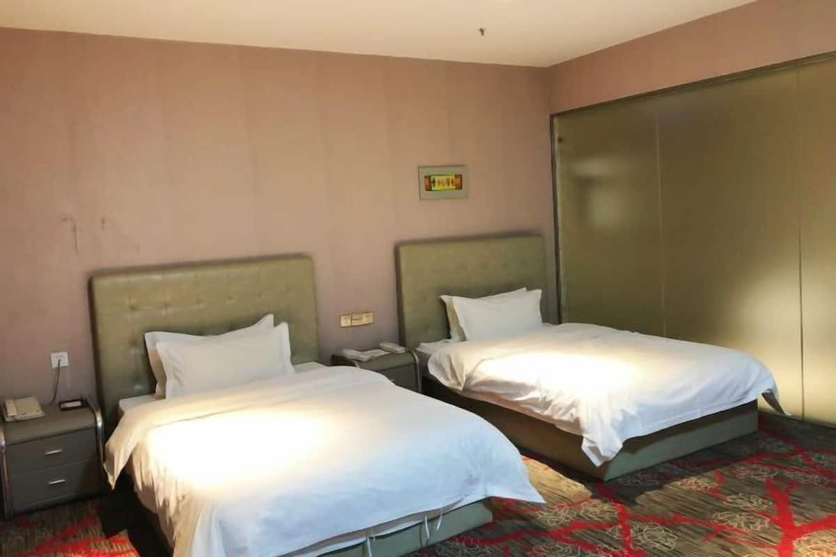 A hotel room with two beds, a wardrobe, a bedside table, and a telephone.
