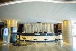 A modern hotel reception area with a curved counter, three staff members, a self-service kiosk, and a large pillar. - Wulanhaote Mengjia Hotel (Ulanhot)