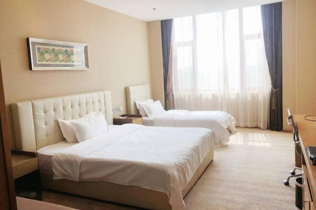 A hotel room with two beds, a desk, a chair, and a large window with curtains.