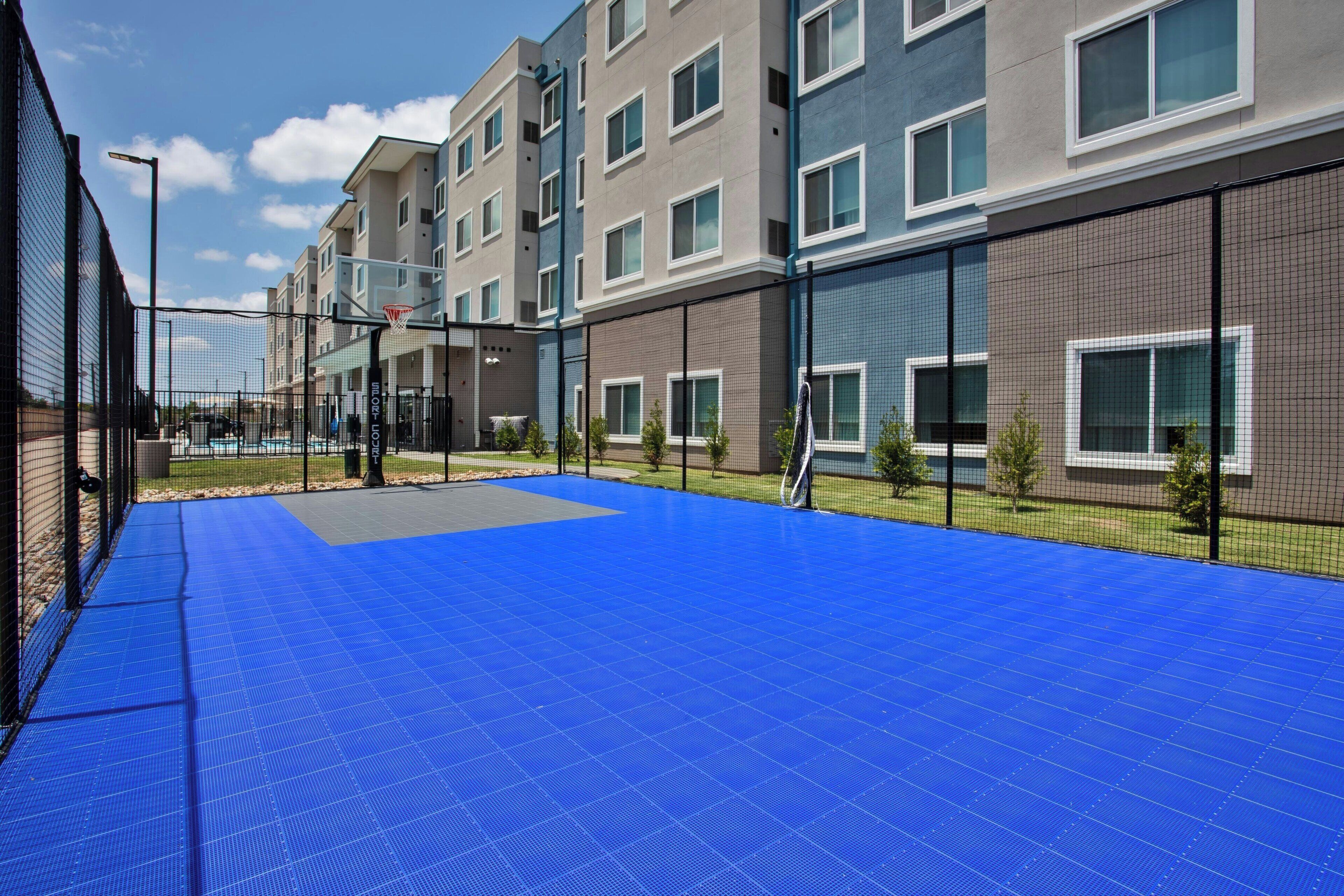 An outdoor basketball court adjacent to a multi-story residential building with a blue floor.