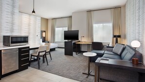 Una habitación de hotel moderna con kitchenette, un sofá, un escritorio y un televisor.