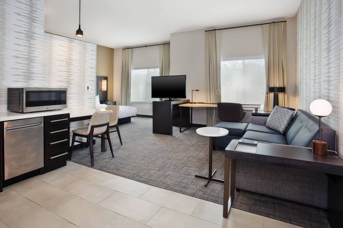 Een moderne hotelkamer met een kitchenette, een bank, een bureau en een televisie.
