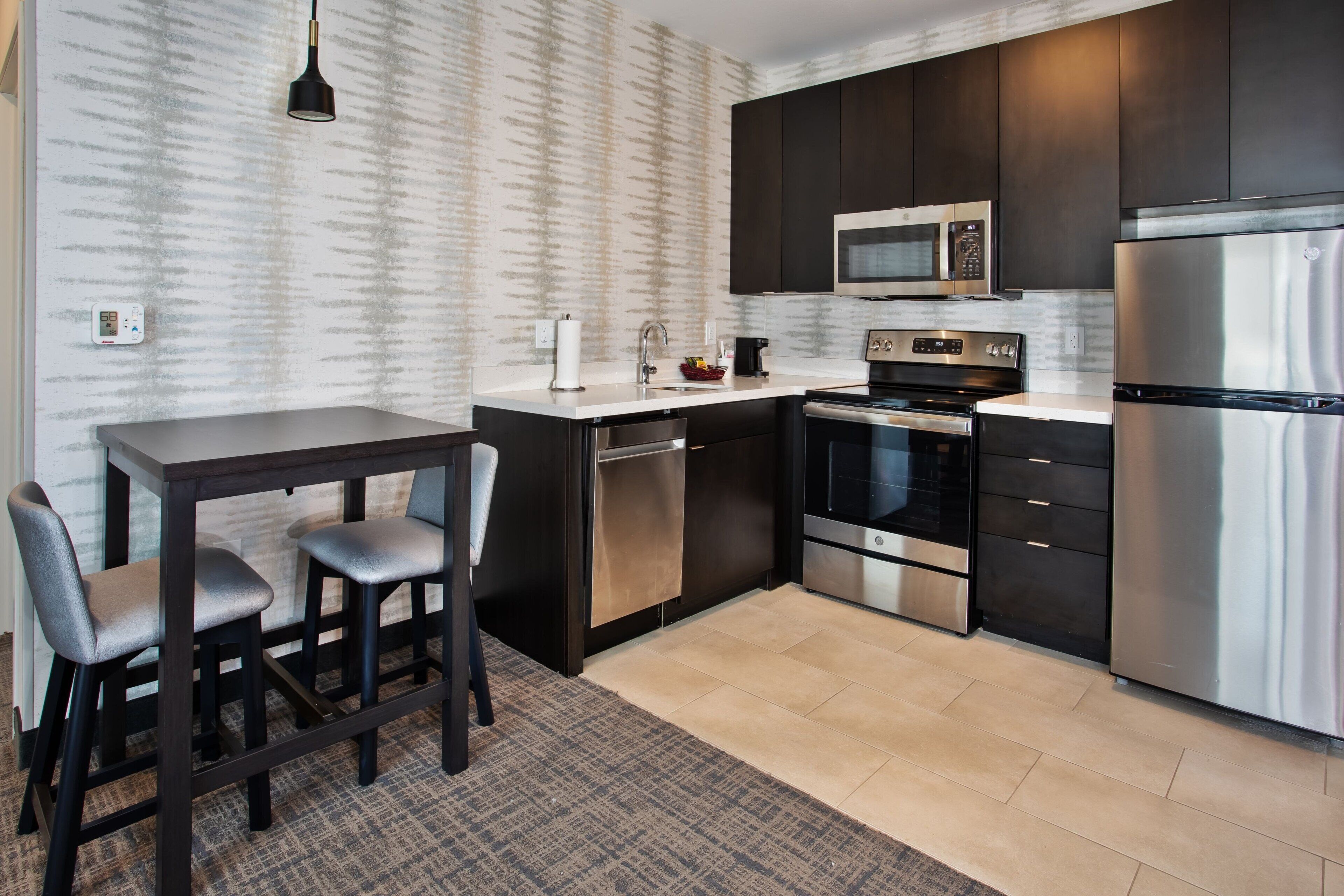 A modern kitchen with dark cabinetry, stainless steel appliances, and a marble countertop.