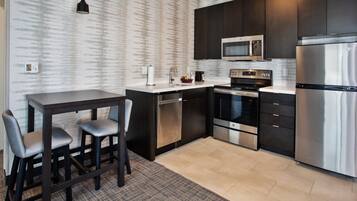 A modern kitchen with dark cabinetry, stainless steel appliances, and a marble countertop.