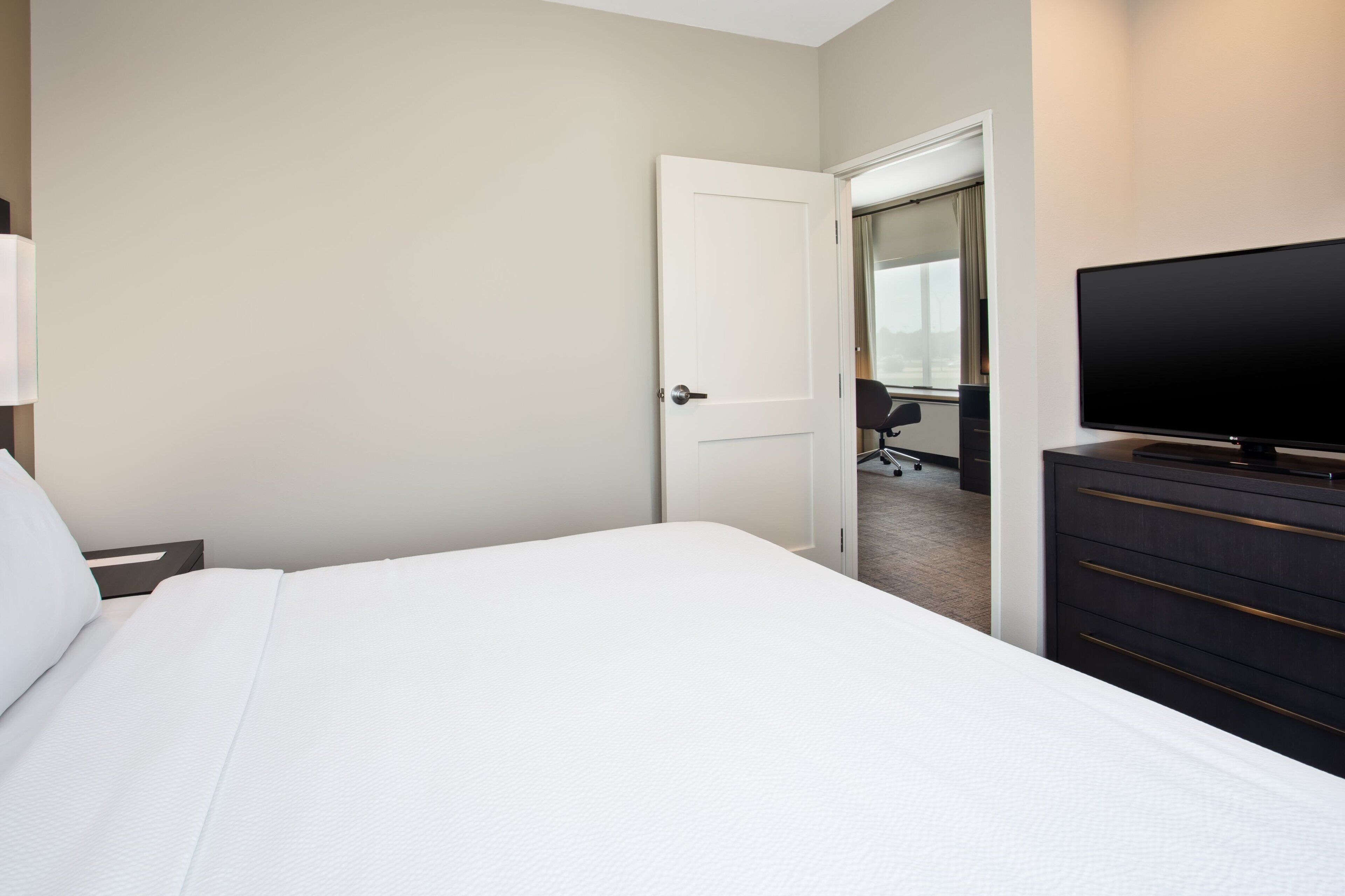 A hotel room with a large bed, a TV on a dresser, and a door leading to a bathroom.