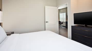 A hotel room with a large bed, a TV on a dresser, and a door leading to a bathroom.