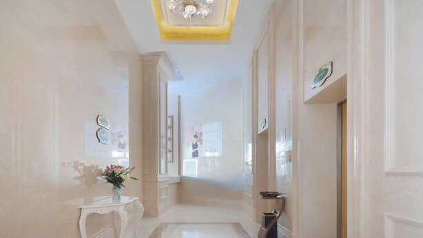 Un couloir orné d’un lustre, une console blanche décorée de fleurs et une poubelle.