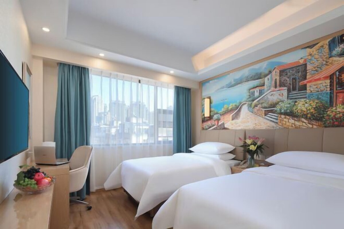 A hotel room with two beds, a desk with a laptop, a chair, and a painting on the wall.