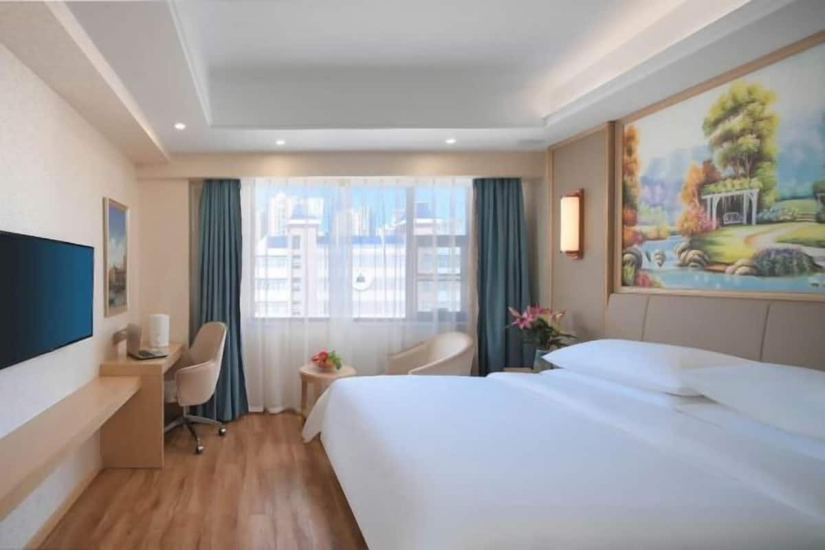 A hotel room with a large bed, a desk with a chair, a TV, and a window with curtains.