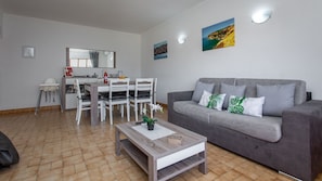 A modern living room with a grey sofa, a wooden coffee table, and a dining area with white chairs and a table.