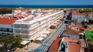 A multi-story hotel with balconies, a central courtyard, and a view of the sea. - 2BD Apartment in Alagoa Beach by LovelyStay (Altura)
