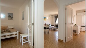 A hotel room with a bed, a chair, a desk, and a bathroom. - 2BD Apartment in Alagoa Beach by LovelyStay (Altura)