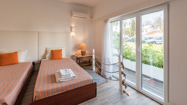 Una camera d'albergo con due letti, un tavolino con una lampada e vista sull'esterno.