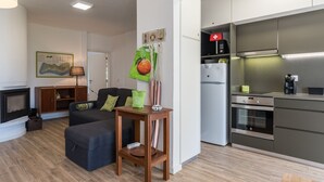 Una sala de estar moderna con chimenea, un sofá, una mesita de madera y una cocina con refrigerador y horno.