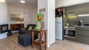 Un salon moderne avec une cheminée, un canapé, une table d’appoint en bois et un coin cuisine équipé d’un réfrigérateur et d’un four.
