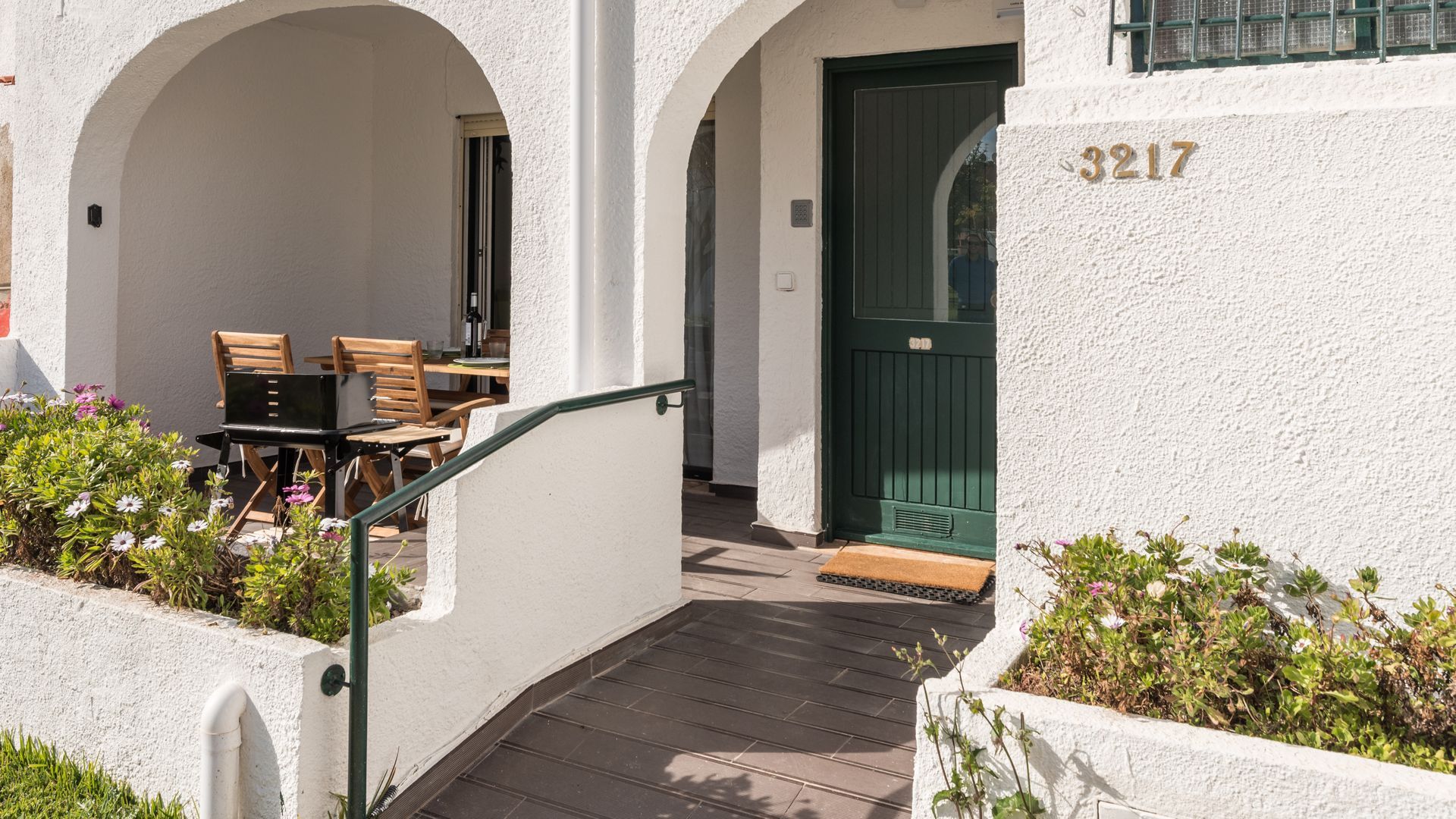 A building with a white exterior, a green door, and the number 3217. There is a staircase leading to an outdoor area with a table and chairs.