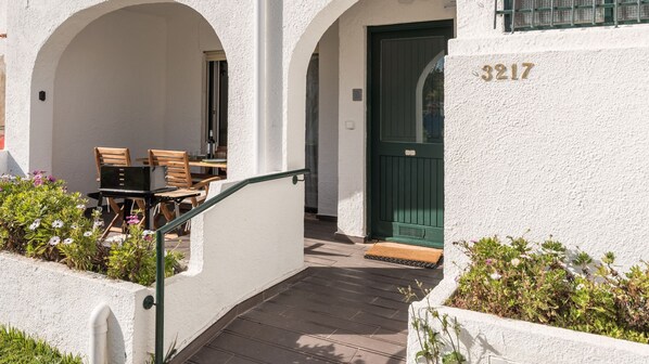 A building with a white exterior, a green door, and the number 3217. There is a staircase leading to an outdoor area with a table and chairs.