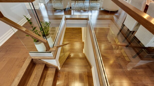 Una escalera moderna con escalones de madera y barandillas de vidrio, que baja a un nivel inferior.