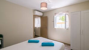 A bedroom with a bed, a wardrobe, an air conditioning unit, a window with curtains, and a door.