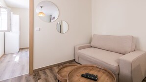 Ein Wohnzimmer mit einem beige farbenen Sofa, zwei runden Spiegeln, einem Holztisch mit einer Fernbedienung und einem Holzboden.
