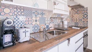 Eine Küche mit Holzarbeitsplatte, Spüle aus Edelstahl, Kaffeemaschine und Toaster. Die Spritzschutzwand zeigt farbige, gemusterte Fliesen.