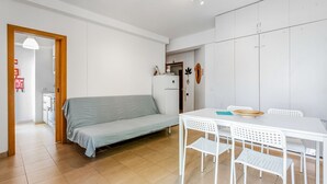 Ett kompakt bostadsutrymme med en soffa, ett matbord med stolar, ett kylskåp och ett litet köksutrymme.