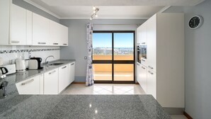A modern kitchen with white cabinets, a granite countertop, and a city view through the sliding glass door.