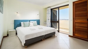 Une chambre à coucher comprenant un lit, une table de chevet, une fenêtre avec des stores et une vue sur l’extérieur.