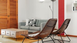 Un salon avec un canapé gris, deux fauteuils marron, une table basse en bois et un lampadaire.