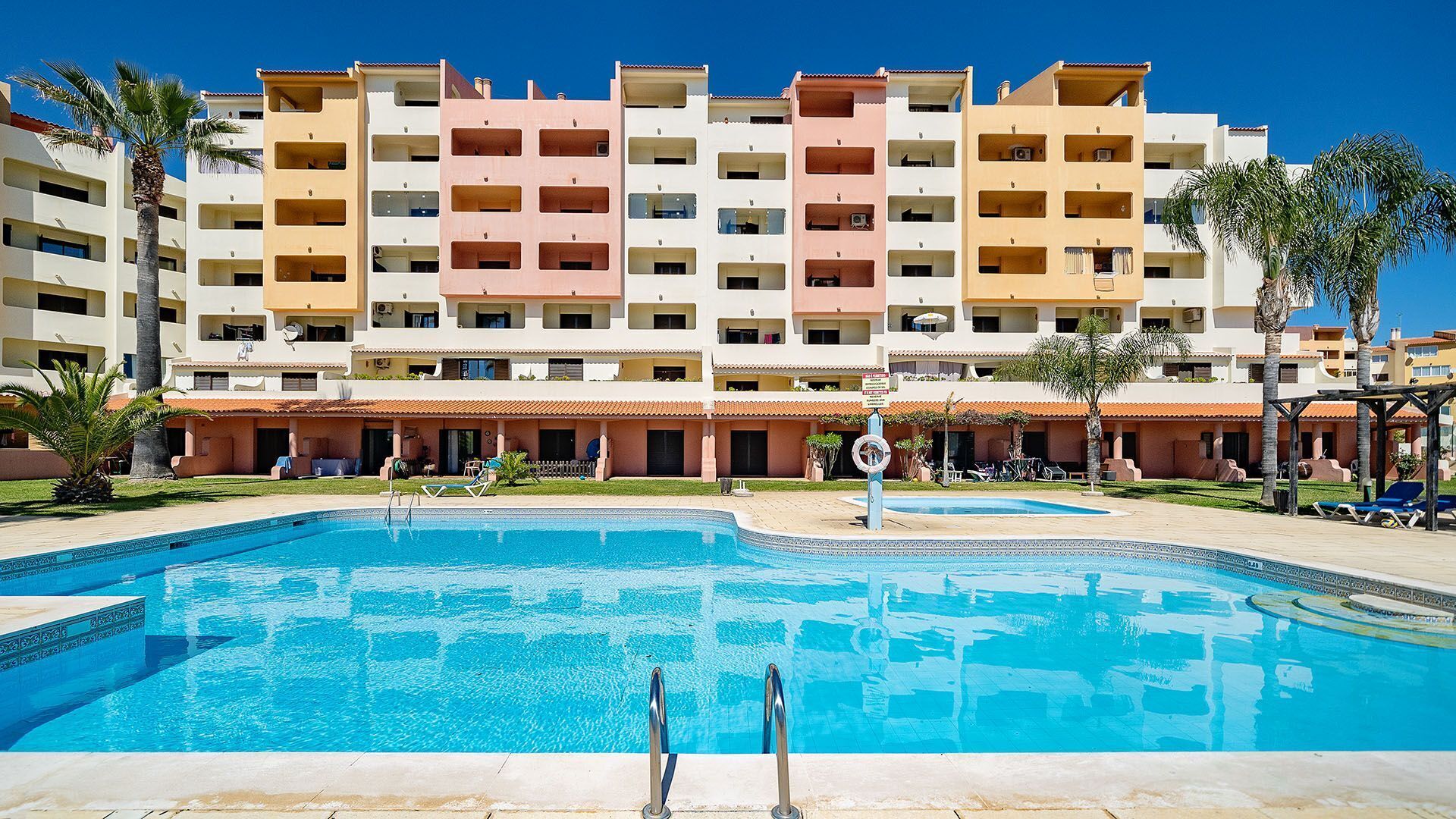 A hotel with multiple balconies, a swimming pool, and palm trees.