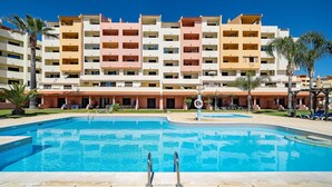 A hotel with multiple balconies, a swimming pool, and palm trees.