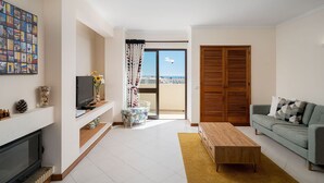 A living room with a TV, sofa, wooden coffee table, and a balcony with a view.