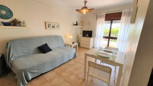 A cozy living room with a sofa, a TV, a dining table with chairs, and a window with curtains. - Lovely Algarvian Escape by LovelyStay (Manta Rota)