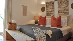 A neatly arranged bedroom with a bed, pillows, a bedside lamp, a woven basket, and a wall hanging. - 2BR  Duplex Townhouse w/Pool by LovelyStay (Ferragudo)