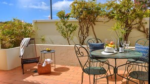 An outdoor patio with a round table, chairs, a basket, and a small table with fruits and a bottle. - 2BR  Duplex Townhouse w/Pool by LovelyStay (Ferragudo)