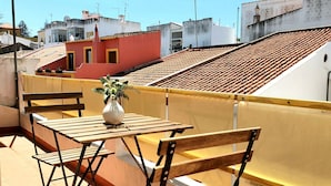En tagterrasse med et træbord og stole, en potteplante og et gult gelænder.