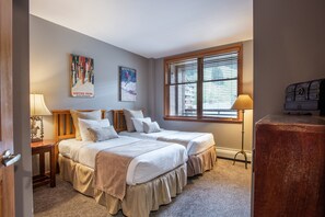 Une chambre avec deux lits, une fenêtre avec des stores, une lampe et une affiche accrochée au mur.