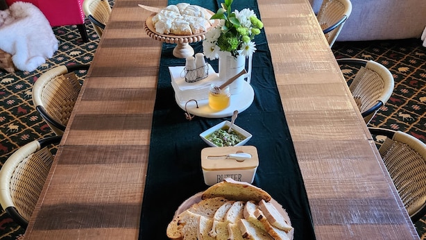 A long wooden table with a black table runner, decorated with bread, a small bowl of jam, a container of butter, and a vase of flowers. - The Carter inn (Ten Sleep)