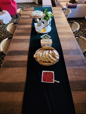 A long wooden table with a black table runner, decorated with bread, a small bowl of jam, a container of butter, and a vase of flowers. - The Carter inn (Ten Sleep)