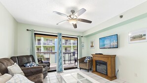 Un salon doté d’un ventilateur de plafond, d’une cheminée, d’un téléviseur et offrant une vue sur un balcon avec une balustrade.