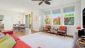 Una sala moderna con un sofá rojo, un comedor con una mesa y sillas, un ventilador de techo y ventanas amplias con vistas a zonas verdes.