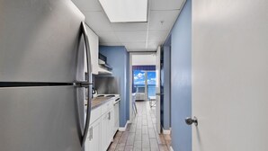 A narrow hallway with a stainless steel refrigerator, a kitchen area with a stove, and a view of the outdoors through a door. - Boardwalk Resort Condo Ocean-front Balcony 🏊 Pool 🏊 (Myrtle Beach)