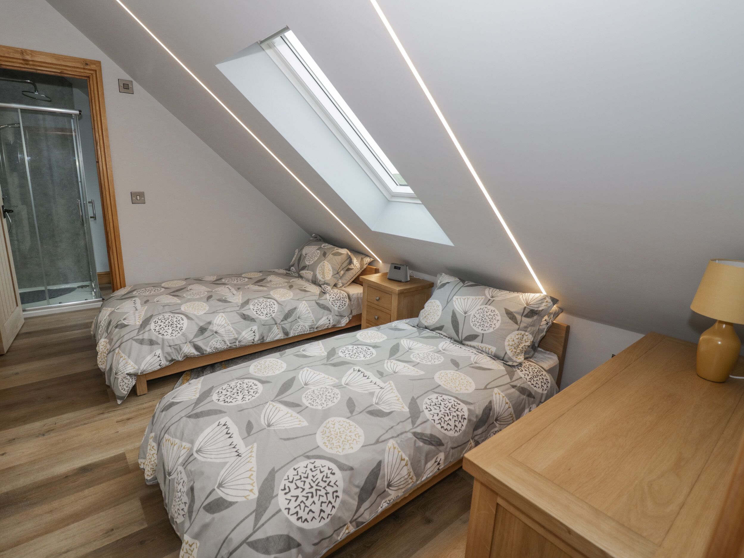 A bedroom with two beds, a skylight, a wooden nightstand, and a bedside table.